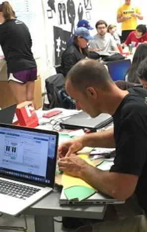 person working at a laptop in a busy maker lab